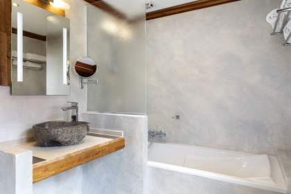 Salle de bain élégante avec vasque en pierre sur plan de travail en bois, miroir éclairé, paroi en verre dépoli et baignoire moderne