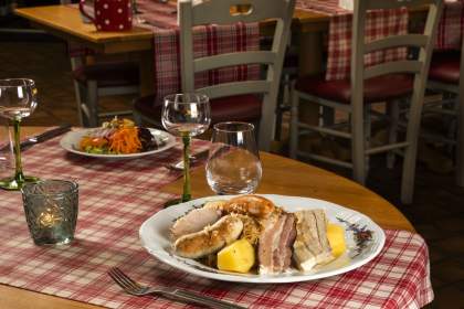 Assiette de choucroute garnie avec saucisses, morceaux de viande et pommes de terre, posée sur une table en bois avec nappe à carreaux rouges et verres à pied
