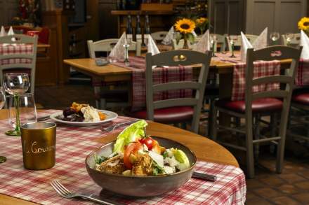 A plate of salad topped with fresh vegetables and croutons on a table laid with a red chequered tablecloth, in a restaurant decorated with sunflowers
